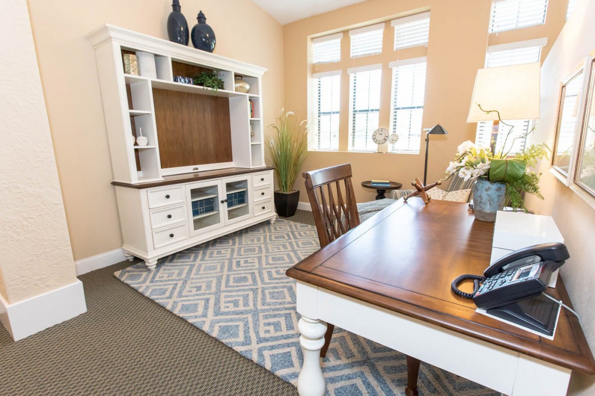 A cozy home office with a wooden desk, chair, and a large window letting in natural light.