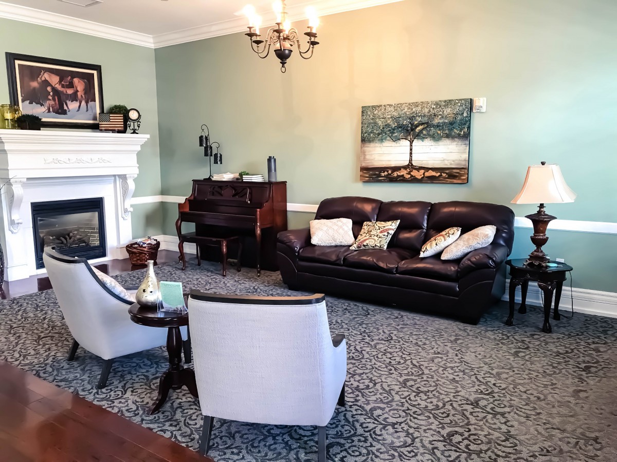 A cozy living room featuring a leather sofa, two armchairs, and a piano, accented by a fireplace and artwork on the wall.
