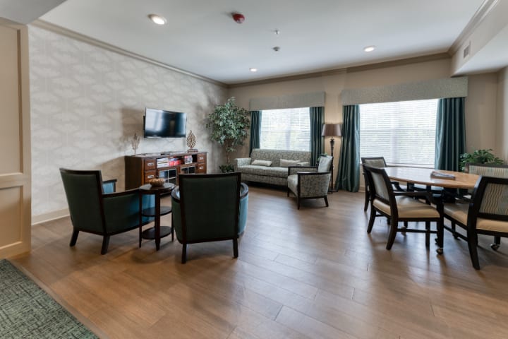 A comfortable living room with modern furnishings, featuring a television, seating area, and large windows with curtains.