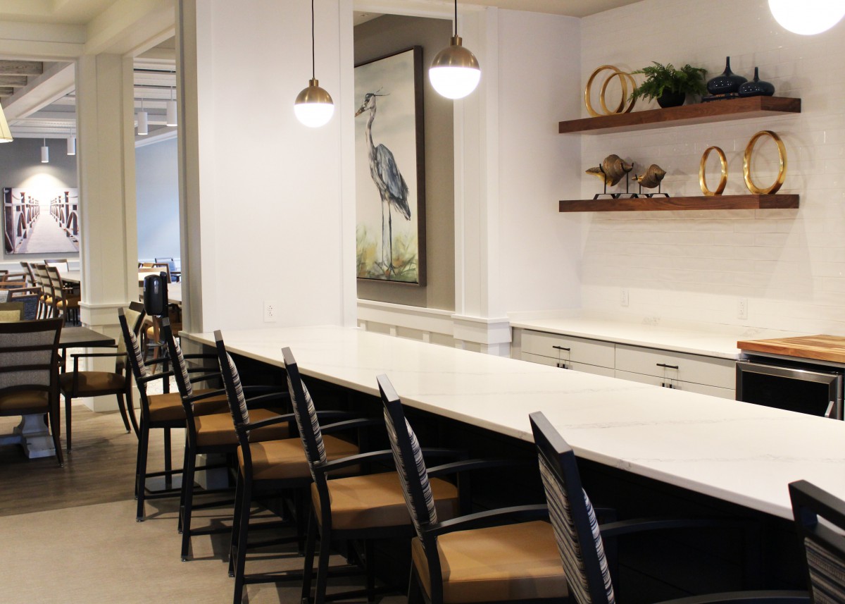 Modern kitchen with a long countertop and seating area, accented by pendant lights and decorative shelves.