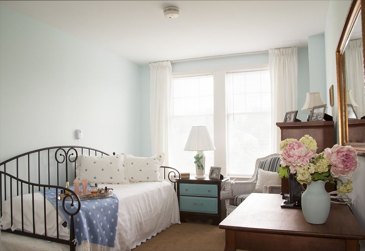 A bright and cozy bedroom featuring a daybed with decorative pillows, a side table with a lamp, and a floral arrangement on the coffee table.