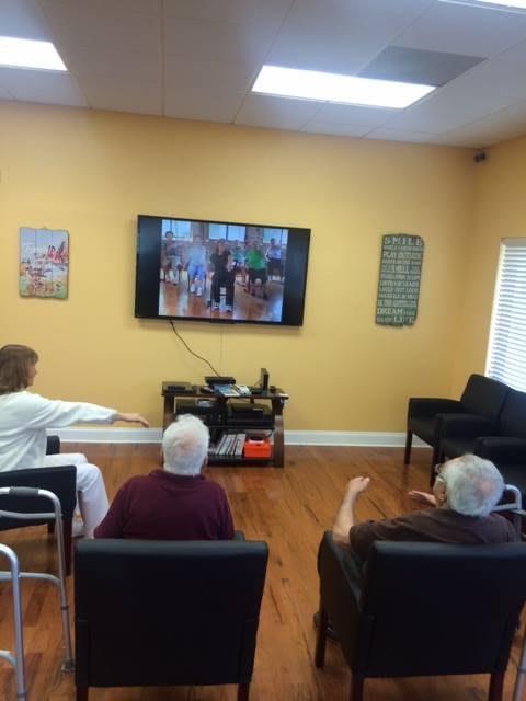 Seniors participating in a group exercise session while watching a program on television.