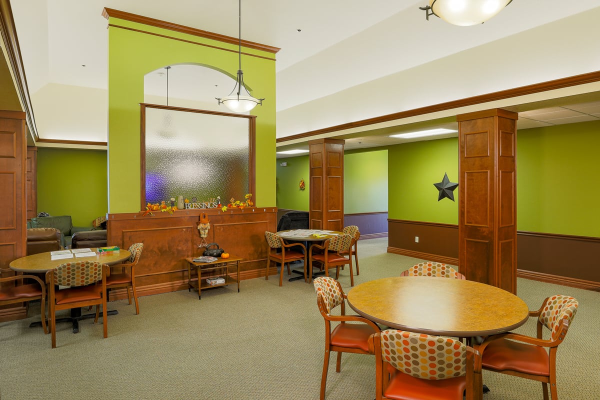 A cozy dining area with round tables and wooden decor, featuring green walls and elegant lighting.