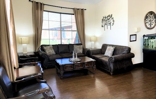 A cozy living room featuring dark leather sofas, a wooden coffee table, and soft natural light filtering through the curtains.