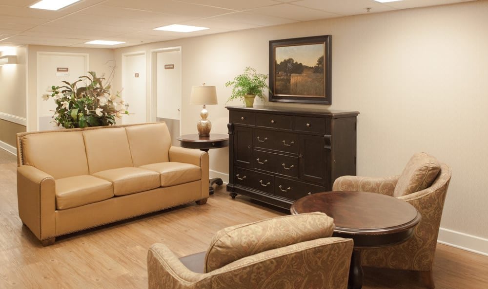 A cozy living room with a beige sofa, armchairs, dark wooden cabinet, and wall art.