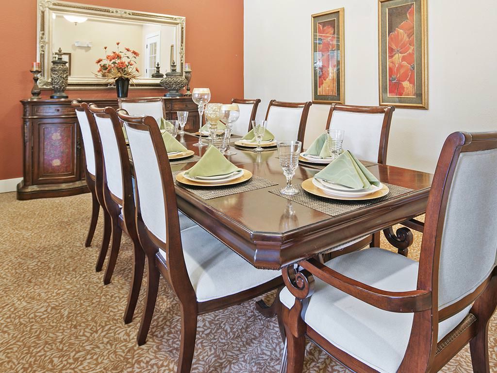 An elegant dining room with a large wooden dining table, neatly set with green napkins and glassware.