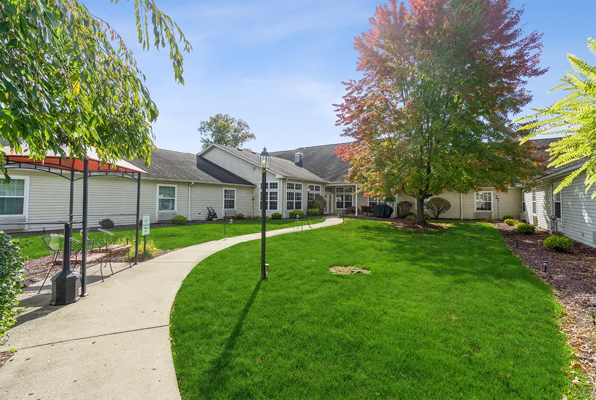 A scenic view of a building surrounded by green lawns and trees, with a pathway leading to the entrance under a clear blue sky.