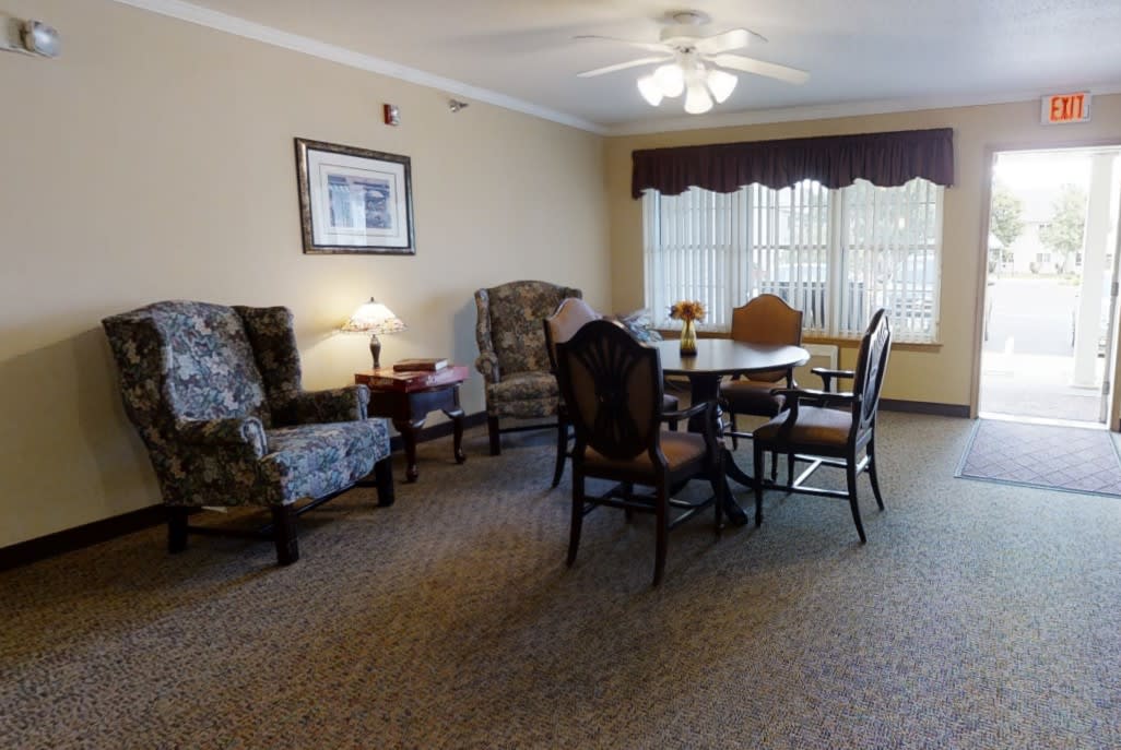 A cozy living room with a dining table and chairs, a lamp, and comfortable armchairs, decorated with artwork on the wall.