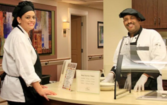 Two people in uniform smiling at a reception desk.