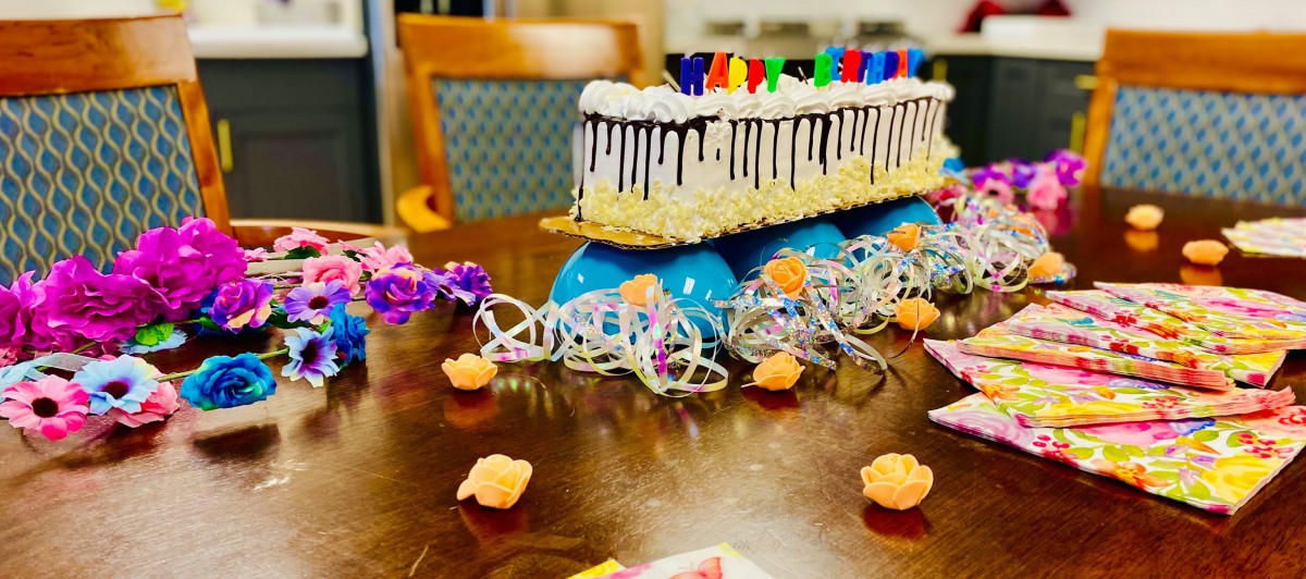 A festive birthday setup featuring a cake with colorful candles and decorative elements on a table.