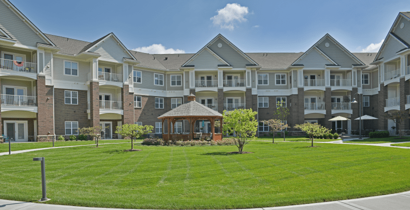 A residential apartment building with a well-maintained lawn and a gazebo under a clear sky.