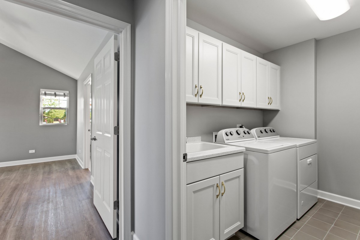 A modern laundry room with white cabinets and appliances.