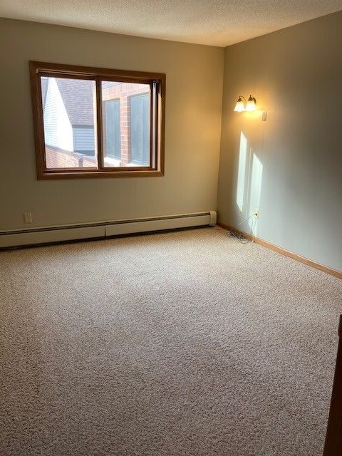An empty room with a carpeted floor, featuring a window and wall lamp.