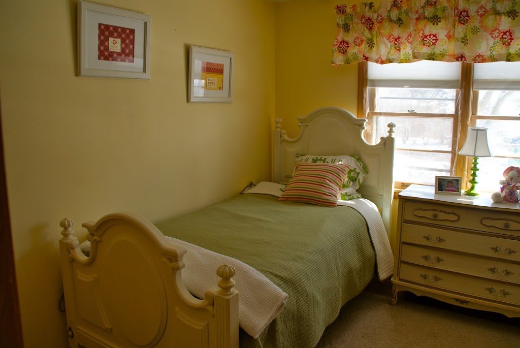A cozy bedroom with a single bed, yellow walls, and colorful decor.