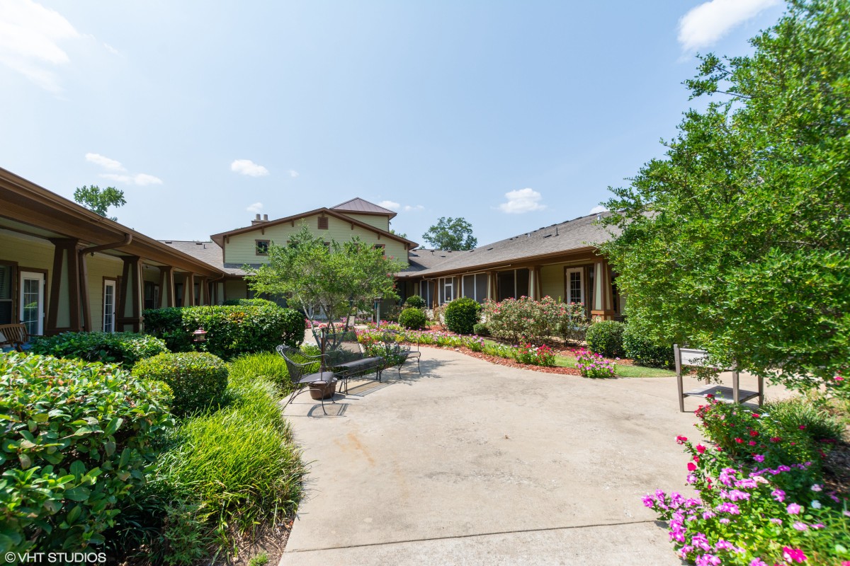A scenic courtyard with lush greenery, benches, and a central pathway leading to a building.