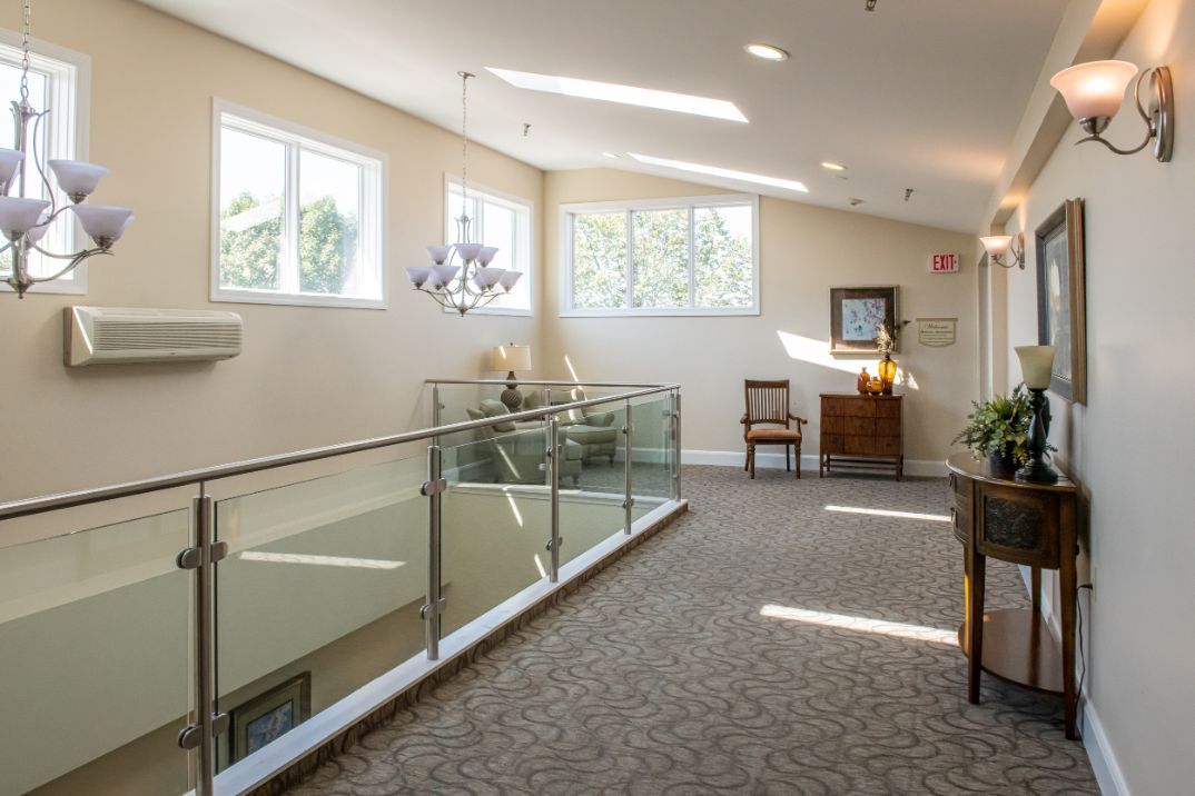 A well-lit hallway with glass railings, a chandelier, and stylish furnishings.