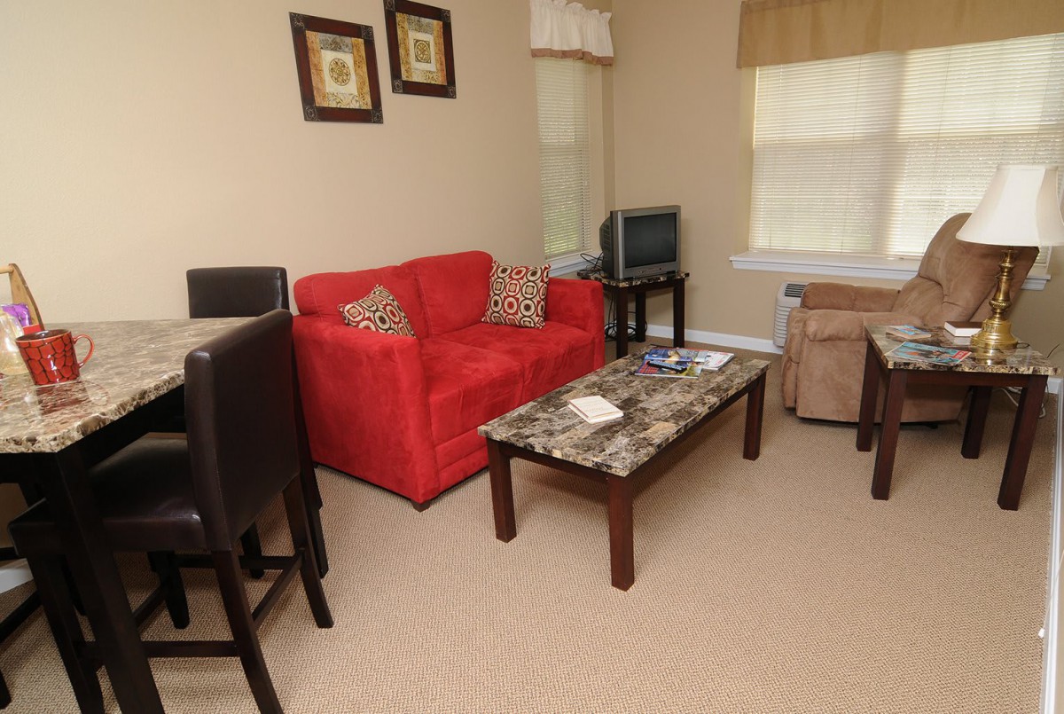 A cozy living room with a red sofa, marble coffee table, and a TV on a stand.