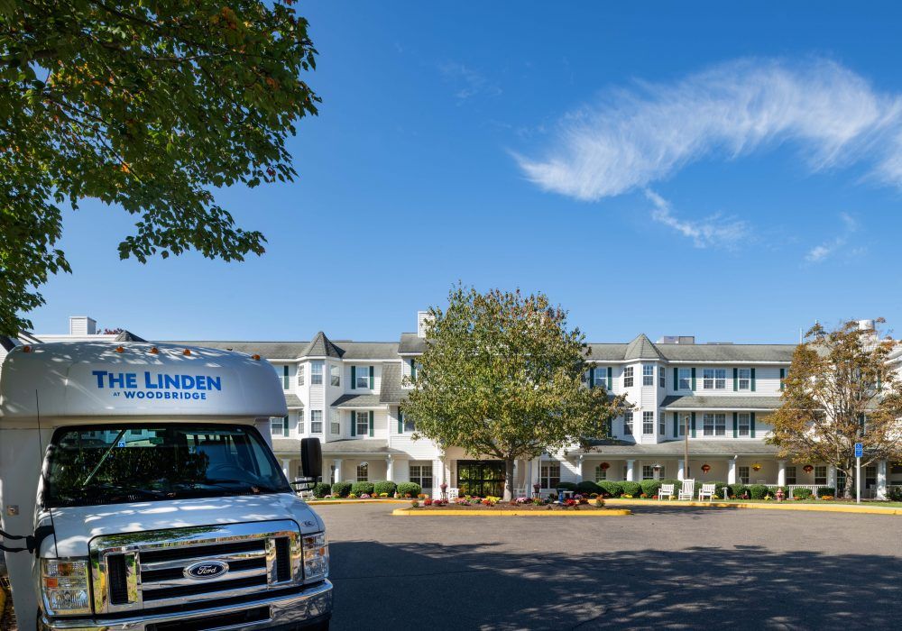 A white multi-story building with a parked van in front, surrounded by trees and under a clear blue sky.