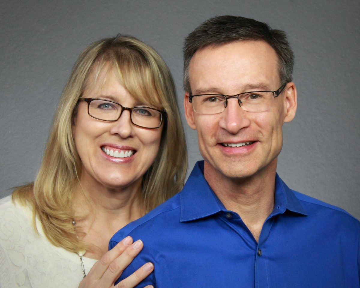A smiling couple posing for a portrait with glasses.