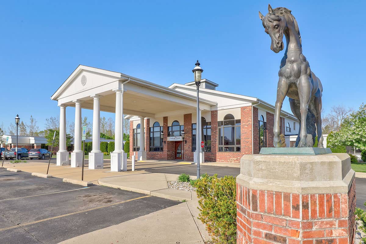 A building entrance featuring a horse statue and classical columns under a clear sky.