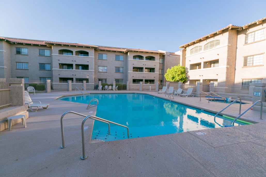 An outdoor swimming pool in the courtyard of an apartment complex under a clear blue sky.