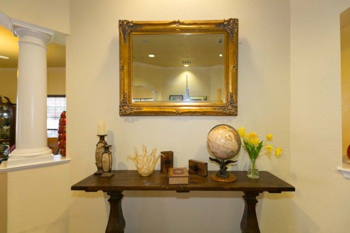 A vintage-style hallway setup with a framed mirror, decorative table, globe, and vase of flowers.