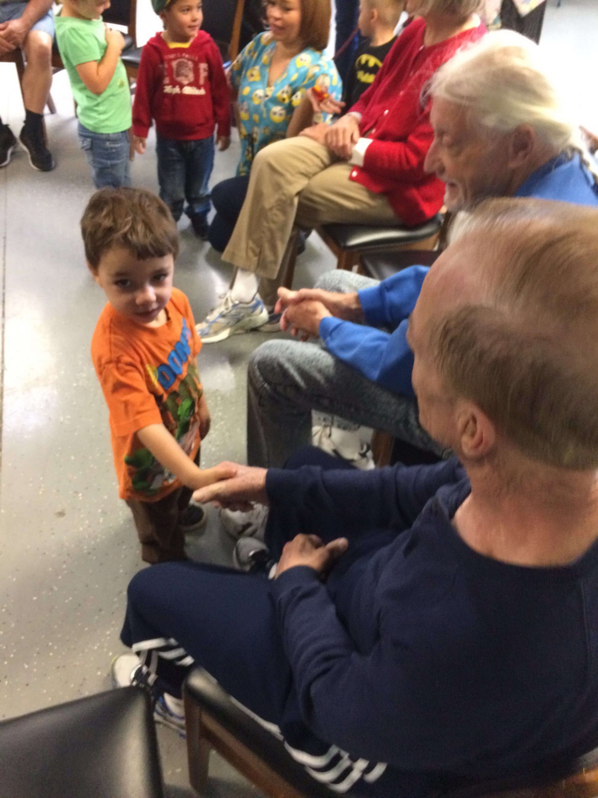 A young child shakes hands with an elderly person, showcasing a heartwarming interaction.