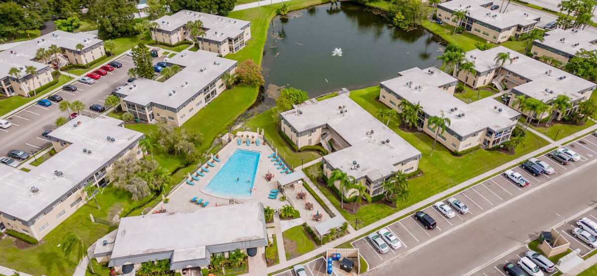 Aerial view of a residential apartment complex with a swimming pool, pond, and green surroundings.