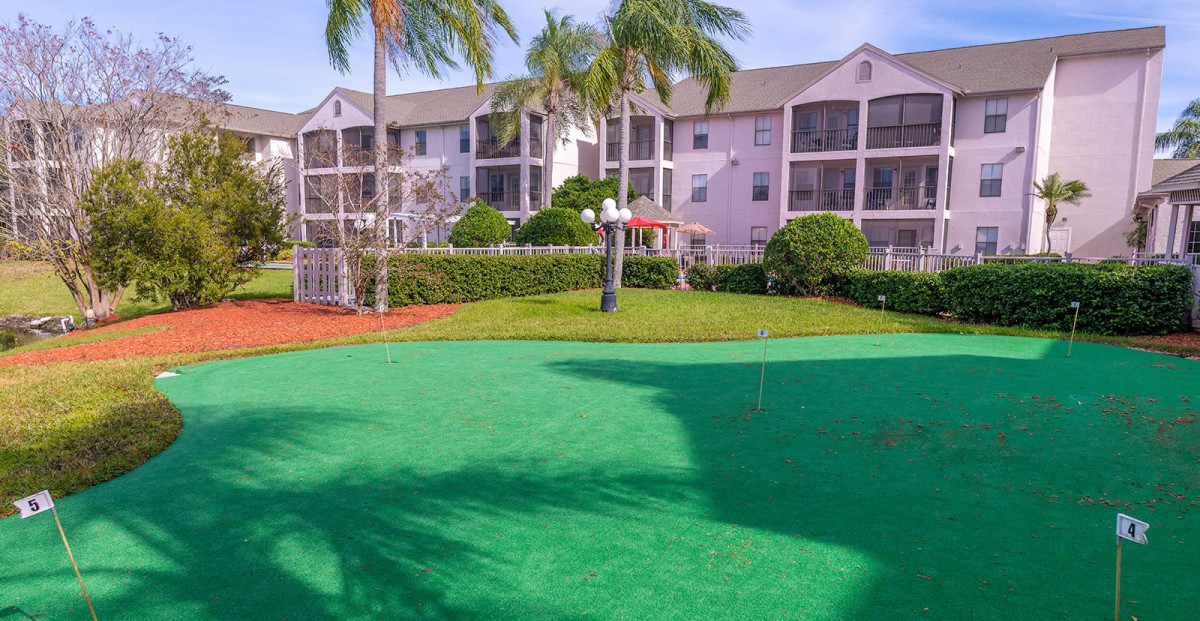 A sunny day view of an apartment complex with a putting green surrounded by palm trees.