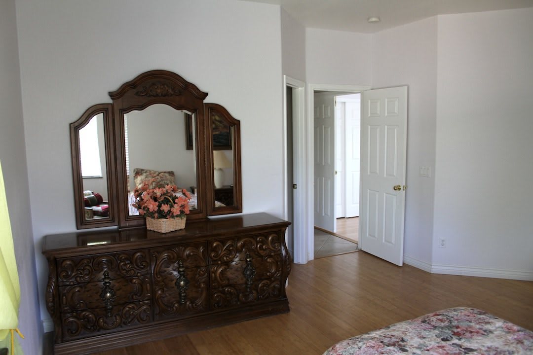A cozy bedroom featuring a wooden dresser with an ornate mirror and a floral arrangement on top.