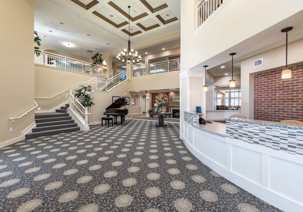 A spacious hotel lobby with a grand staircase, piano, and chandelier.