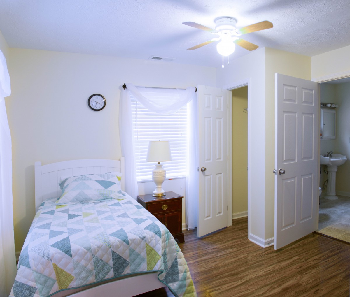 A cozy bedroom with a single bed, lamp, and a ceiling fan.