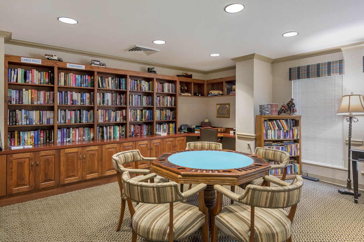 A cozy library room with shelves full of books and a round table surrounded by chairs.