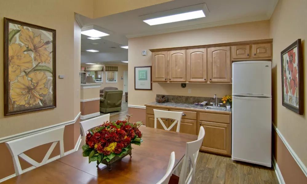 A cozy kitchen and dining area featuring wooden cabinets, a refrigerator, and a dining table adorned with flowers.