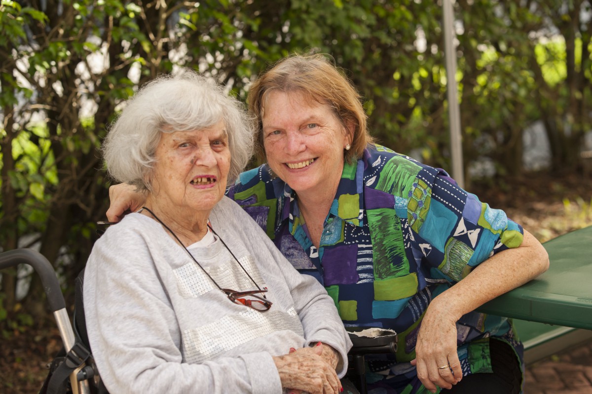 A middle-aged woman and an elderly woman smiling together outdoors.