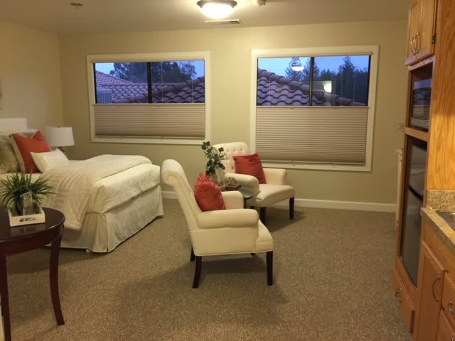 A cozy bedroom with a neatly made bed, two armchairs, and large windows.