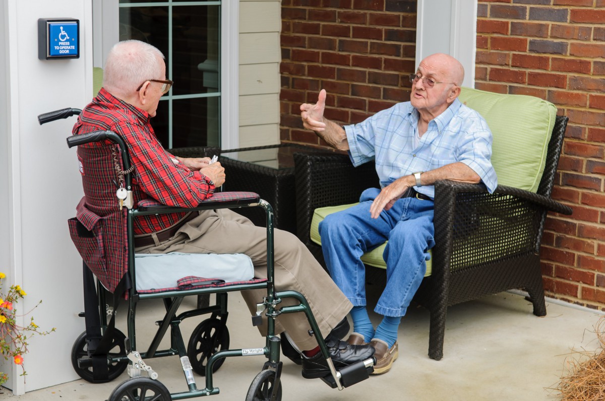 Two elderly men having a conversation outside, one sitting in a wheelchair.