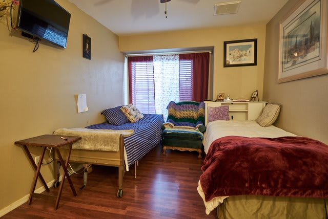 A cozy bedroom featuring two beds with colorful blankets and pillows, a window allowing natural light, and a wooden floor.