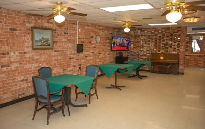 A dining area with tables and chairs against a brick wall, featuring a television and ceiling fans.