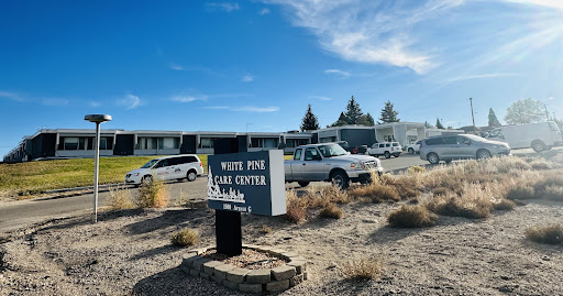 Entrance to White Pine Park Center with vehicles parked outside under a clear blue sky.