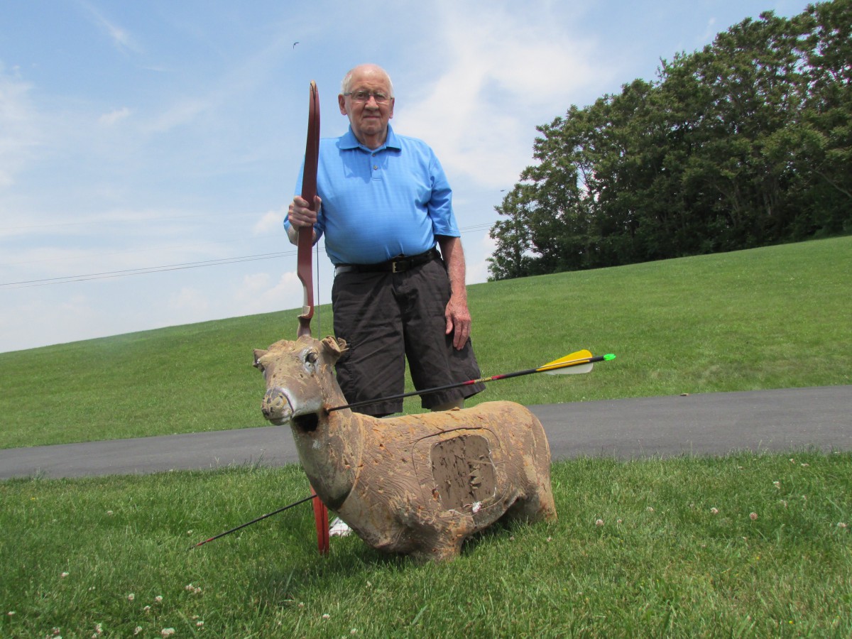 An elderly man practicing archery with a sheep-shaped target in the outdoors.