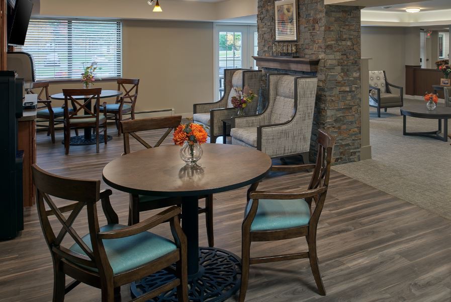 A cozy living room setting featuring a round wooden table with chairs and a vase of flowers, set against a stone-accented wall.