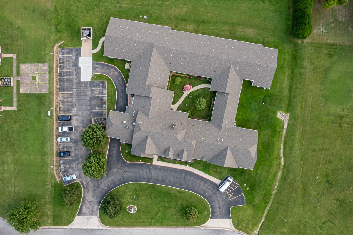 Aerial view of a building with a driveway and adjacent parking lot surrounded by green lawns.