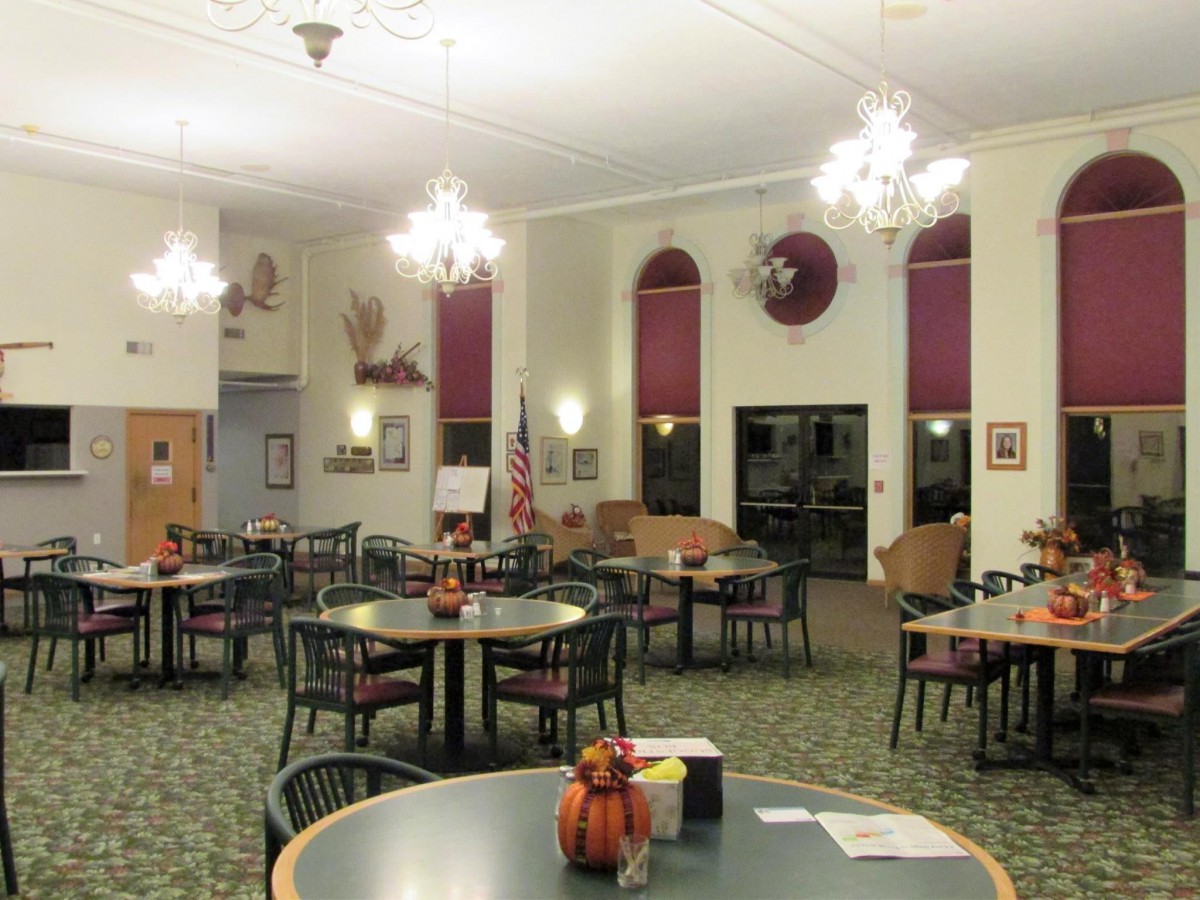 A well-lit dining area with tables and chairs arranged neatly, featuring chandeliers and decorative elements.