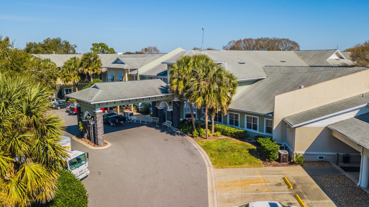 Aerial view of a building entrance with surrounding palm trees and landscaping on a sunny day.