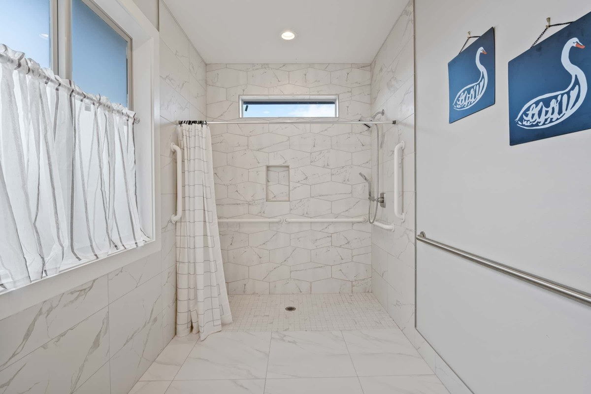 A modern, minimalist bathroom with a marble-tiled walk-in shower area and accessibility features.