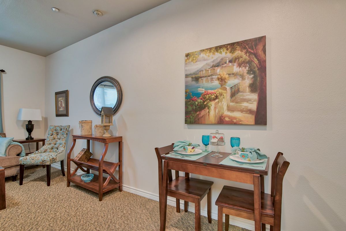 A cozy dining area featuring a wooden table set for two, adorned with teal plates and surrounded by decorative wall art and a mirror.