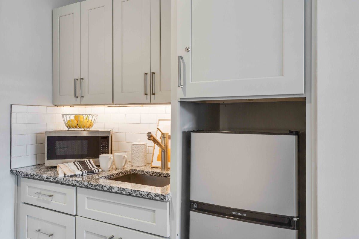 A modern kitchen with white cabinets, a small refrigerator, and various countertop appliances.