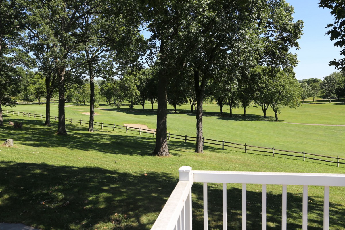 A serene view of a green park with trees and a wooden fence.