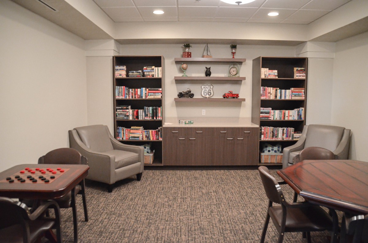 A cozy library with bookshelves, comfortable chairs, and tables in a well-lit room.